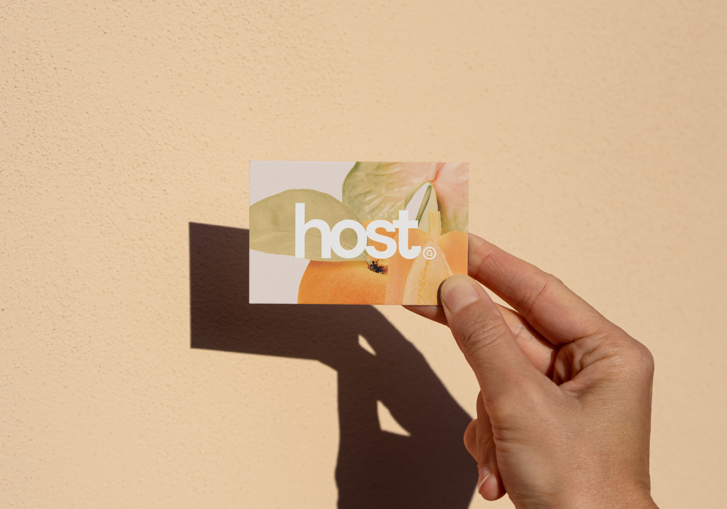 Hand holding a bright business card with fruit and plants on it with the logo for Host Group