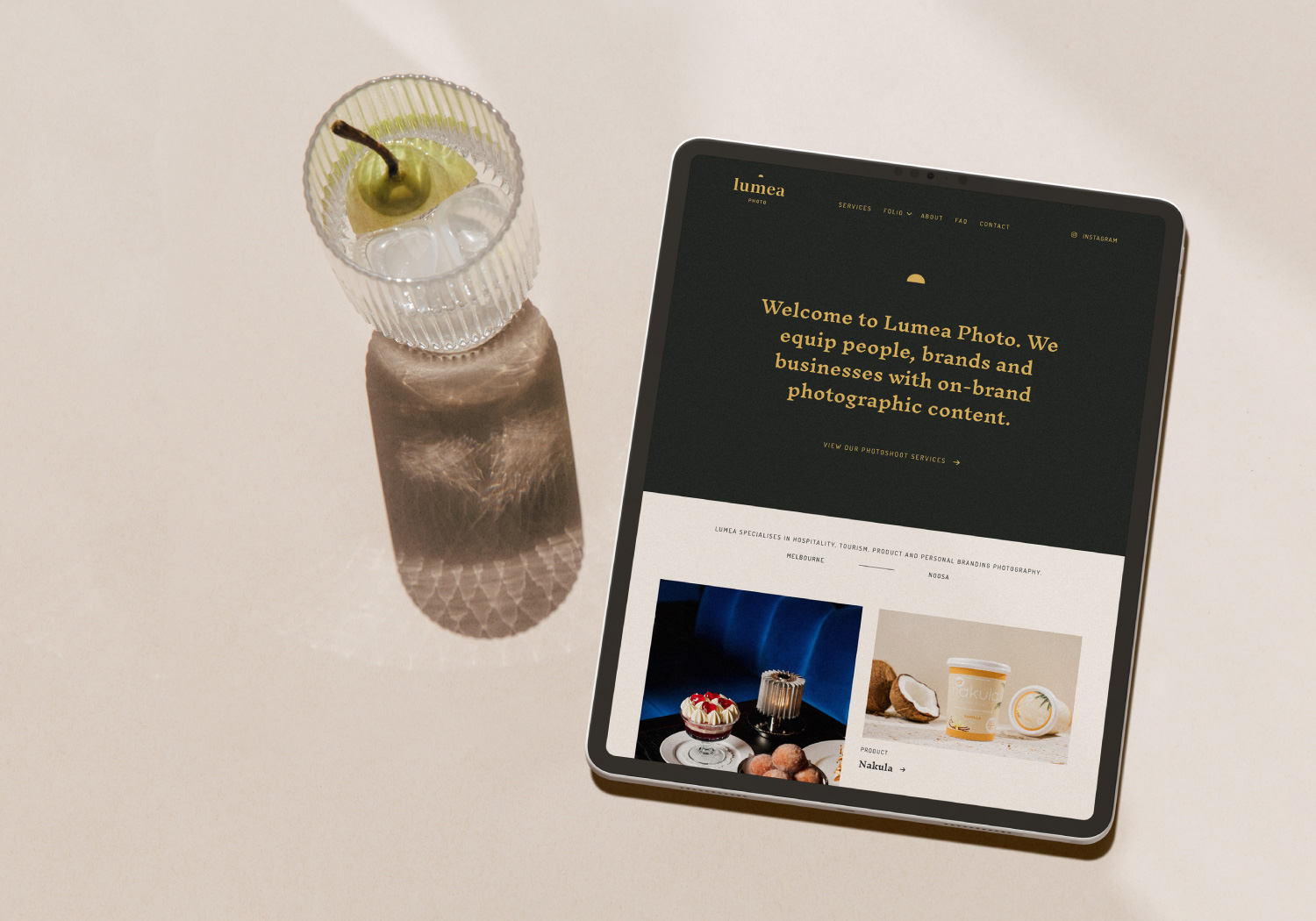 A crystal glass of water and an ipad. The ipad shows the website homepage design for Lumea Photo
