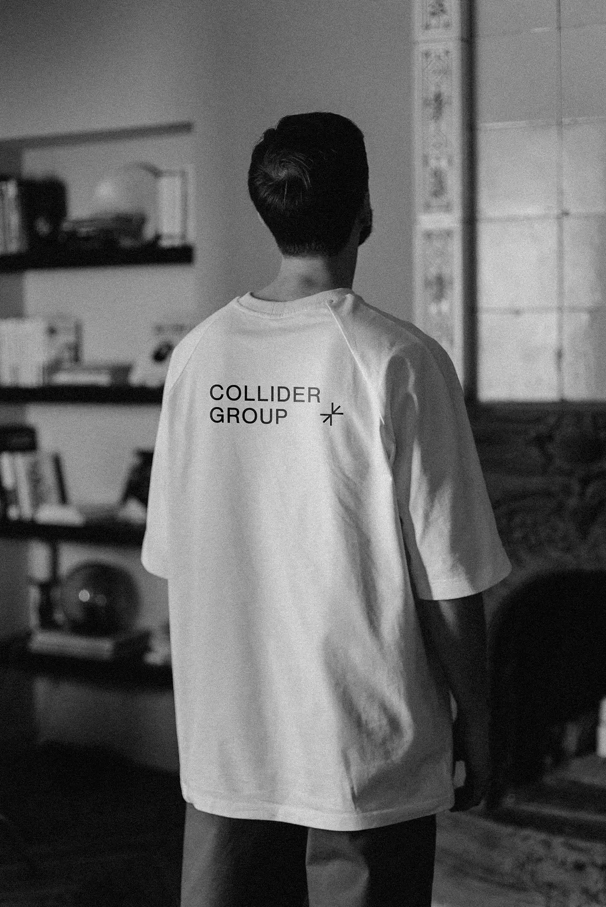 View of a man from behind who is wearing a white shirt with a black Collider Group logo on the back